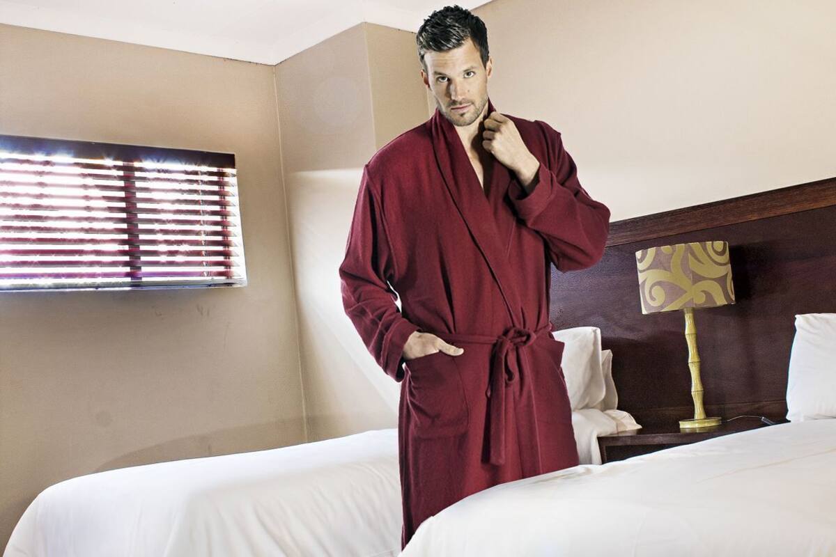 A hotel room with two beds, a wooden floor, a ceiling light, and a window with blinds.