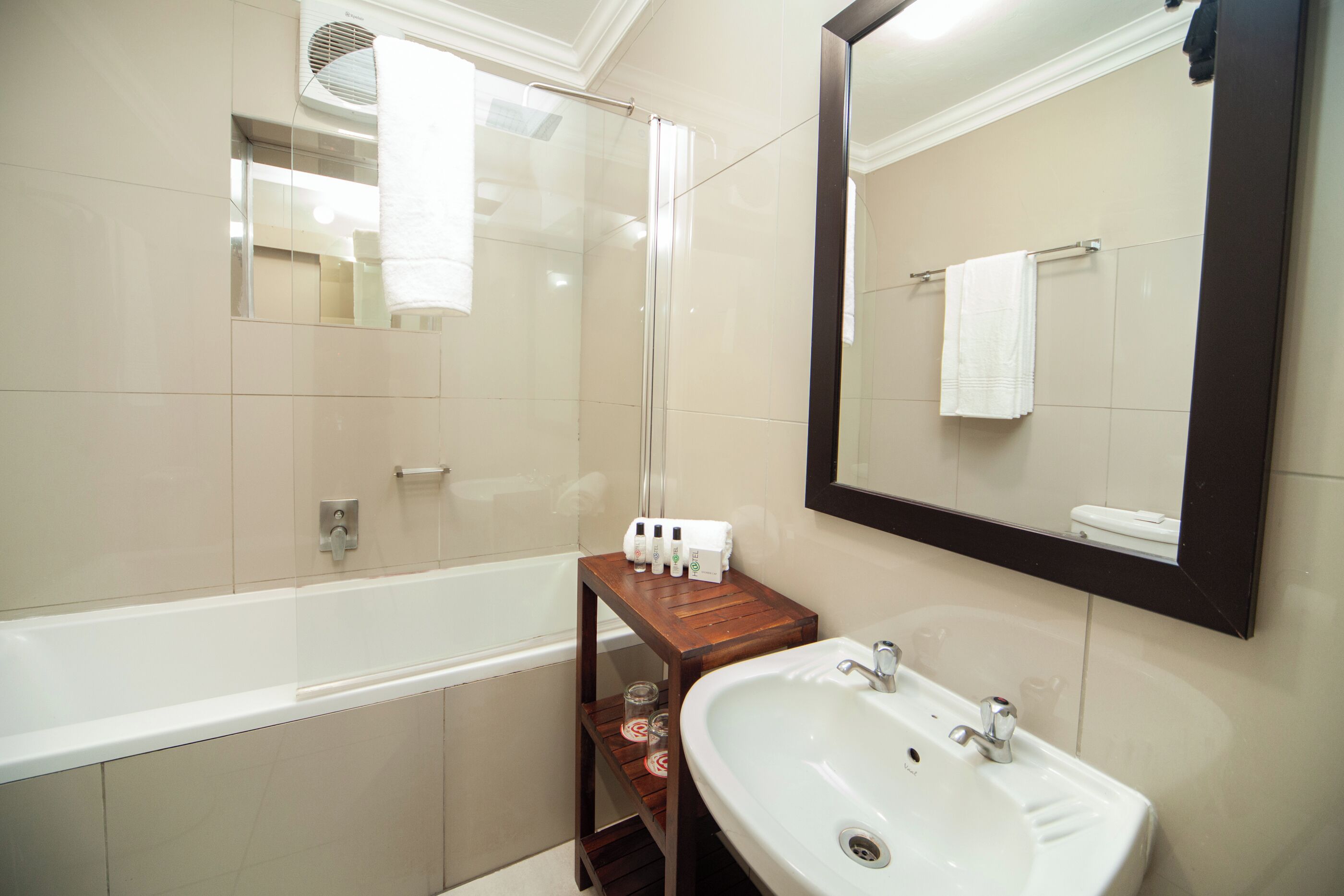 Un baño con una bañera, un lavamanos, un espejo y un estante con artículos de aseo.