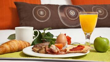 A breakfast setting with croissant, eggs, bacon, toast, orange juice, and an apple on a table.