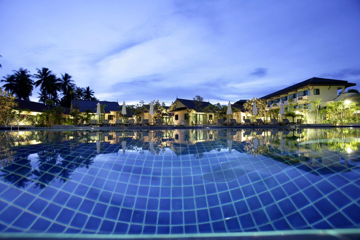 A swimming pool with a tiled surface, surrounded by buildings with multiple floors and balconies, under a twilight sky.