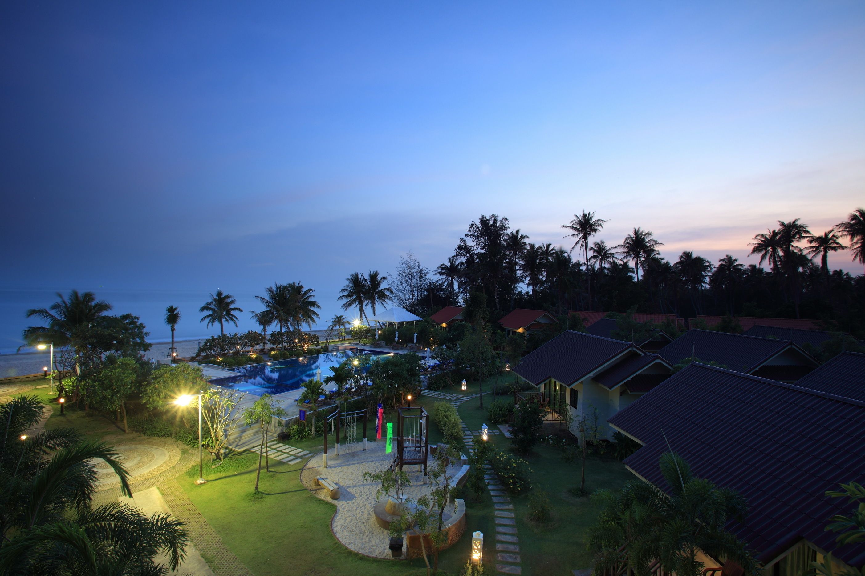 Un resort con piscina, palmeras y senderos bien iluminados.