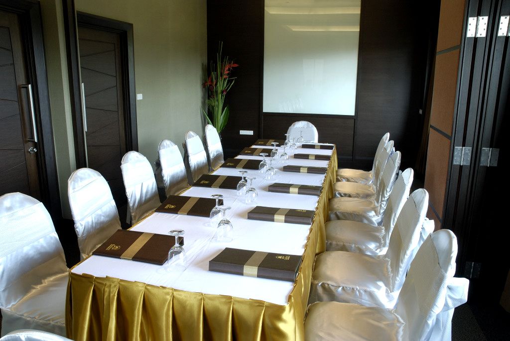 A conference room with a long table, white chairs, and a projector screen.