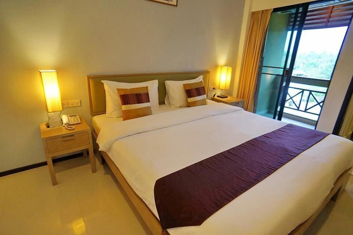 A hotel room with a large bed, bedside lamps, a telephone, and a view of the outdoors through a window.