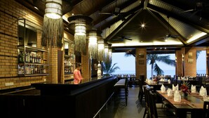 A restaurant with a bar area, wooden tables, and chairs, and a view of palm trees.