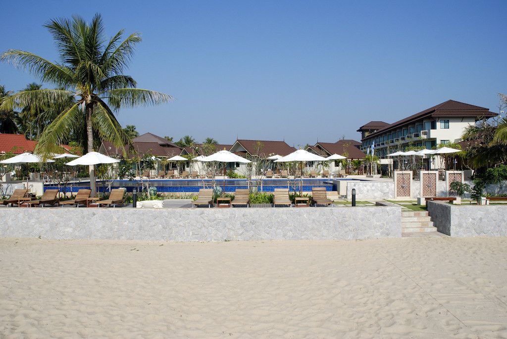 A beachside hotel with sun loungers, umbrellas, and a pool area.