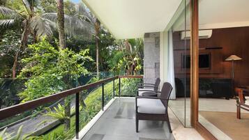 A balcony with a glass railing, a wicker chair, and a view of tropical vegetation.