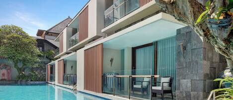 A modern hotel with a swimming pool, balconies with glass railings, and a stone facade.
