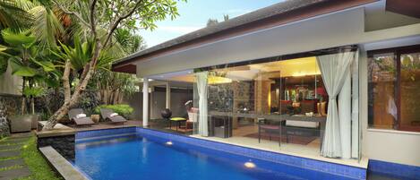 A modern house with a swimming pool, outdoor seating, and lush greenery.