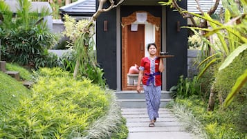A woman walking down a stone pathway towards a building with a dark facade and a wooden door.