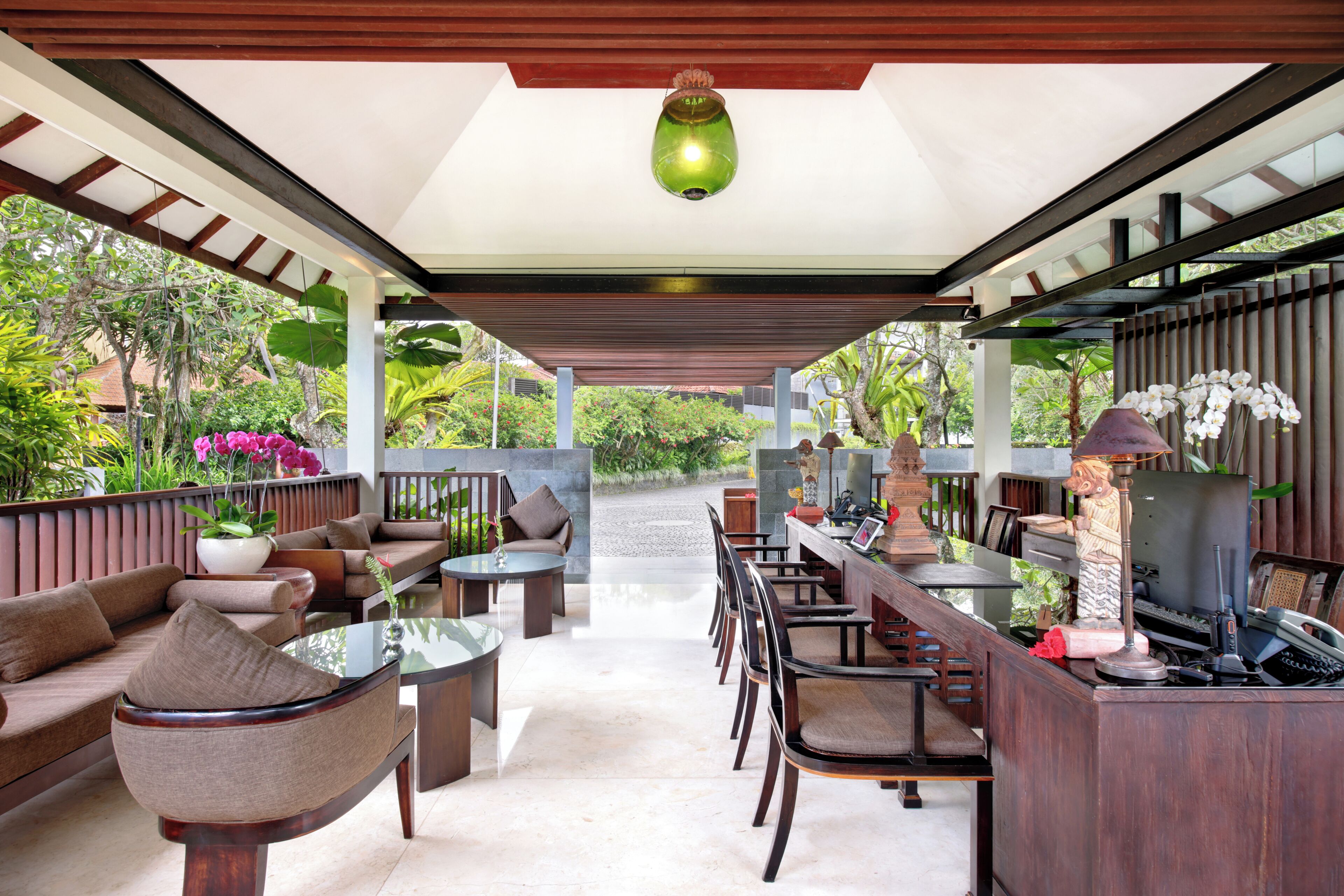 A covered outdoor seating area with sofas, tables, and chairs, surrounded by greenery and a view of the landscape.