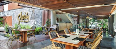 Un restaurant avec des tables et des chaises en bois, un mur en pierre orné d’une enseigne et un escalier menant à un étage supérieur.