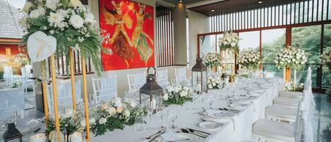 A long table set for a formal event, with white tablecloths, floral centerpieces, and candle holders.