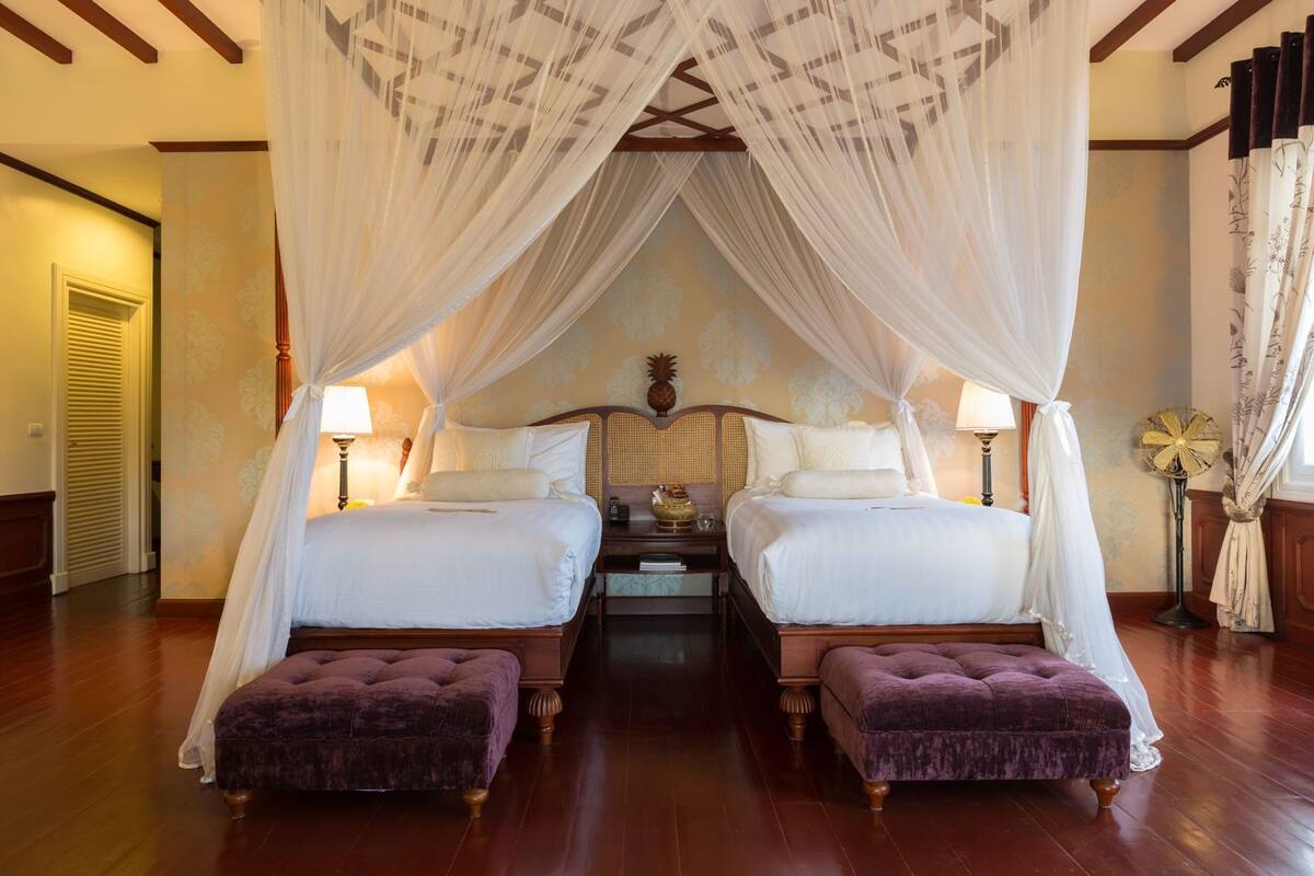 A double bed with a canopy, two bedside tables, and a small table between the beds.