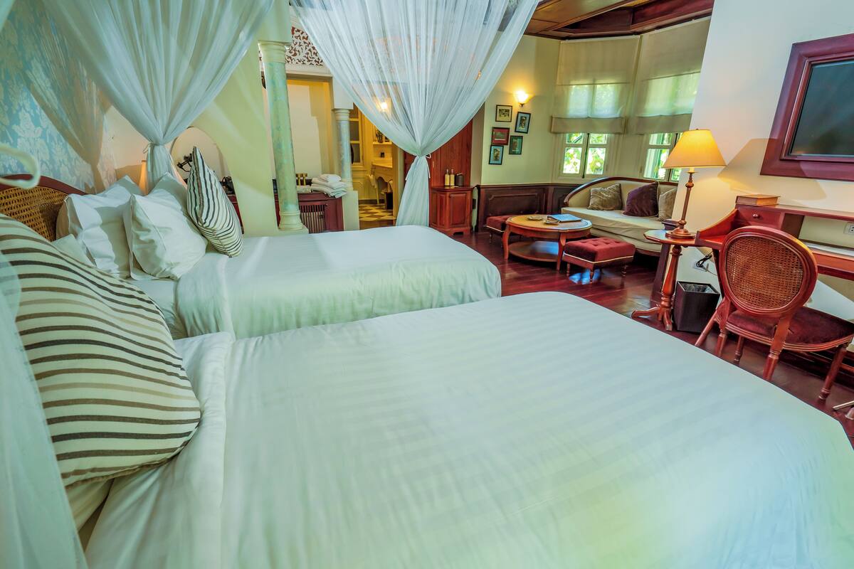 A hotel room with two beds, a sitting area with a table and chairs, and a large window.