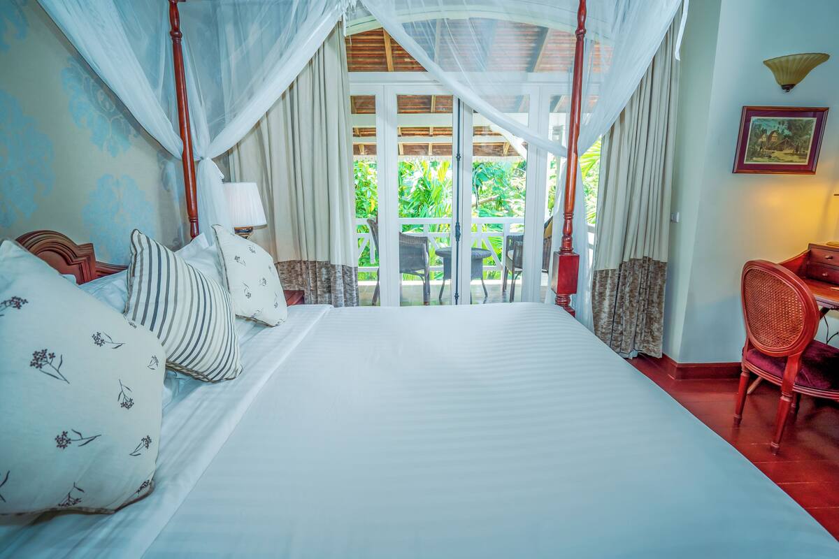 A bedroom with a large bed, a canopy, a desk, and a chair.