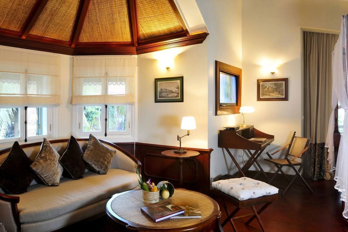 A room with a bed, a sofa, a small table, a chair, and a window with curtains.