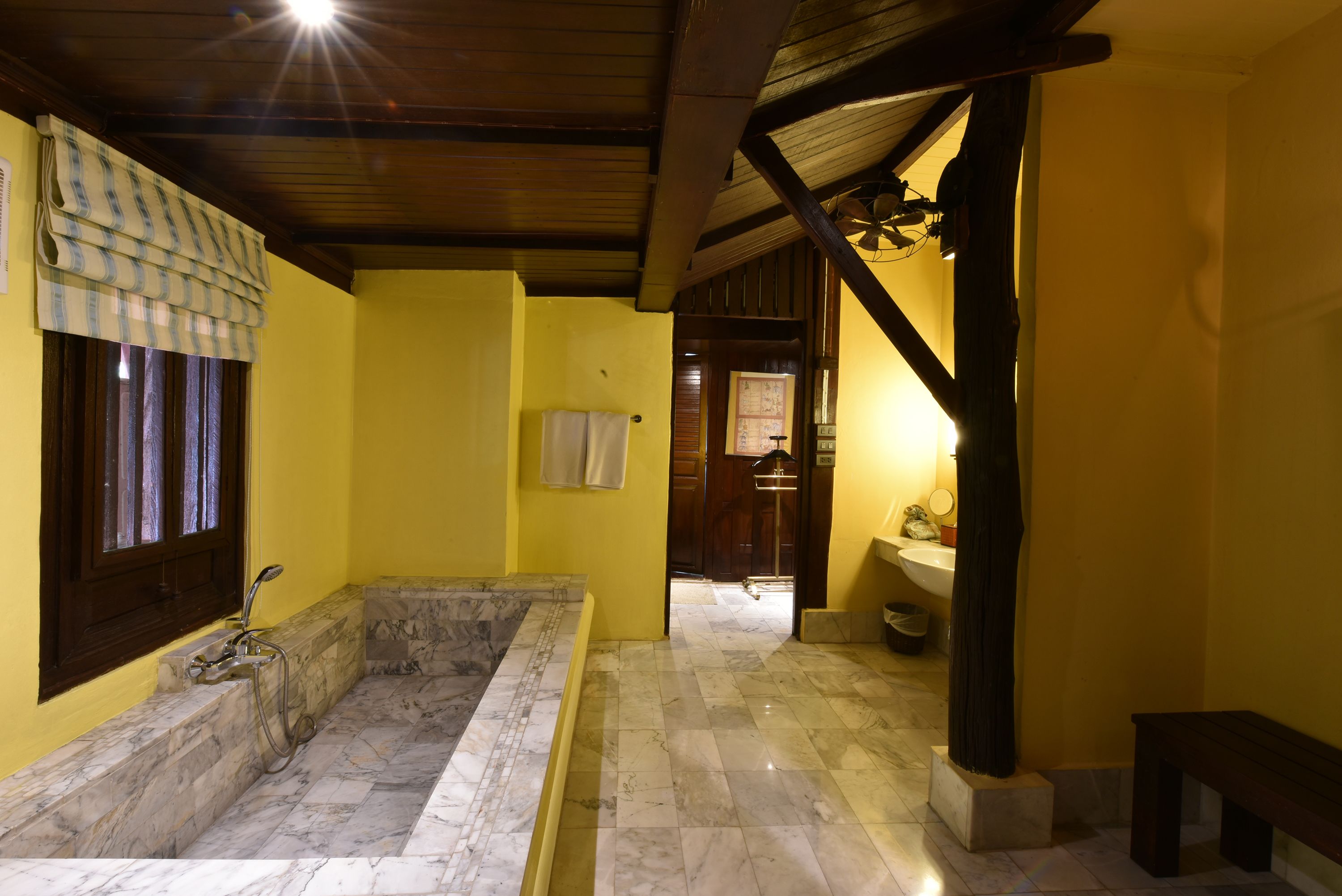 A bathroom with a marble bathtub, yellow walls, and a wooden ceiling.