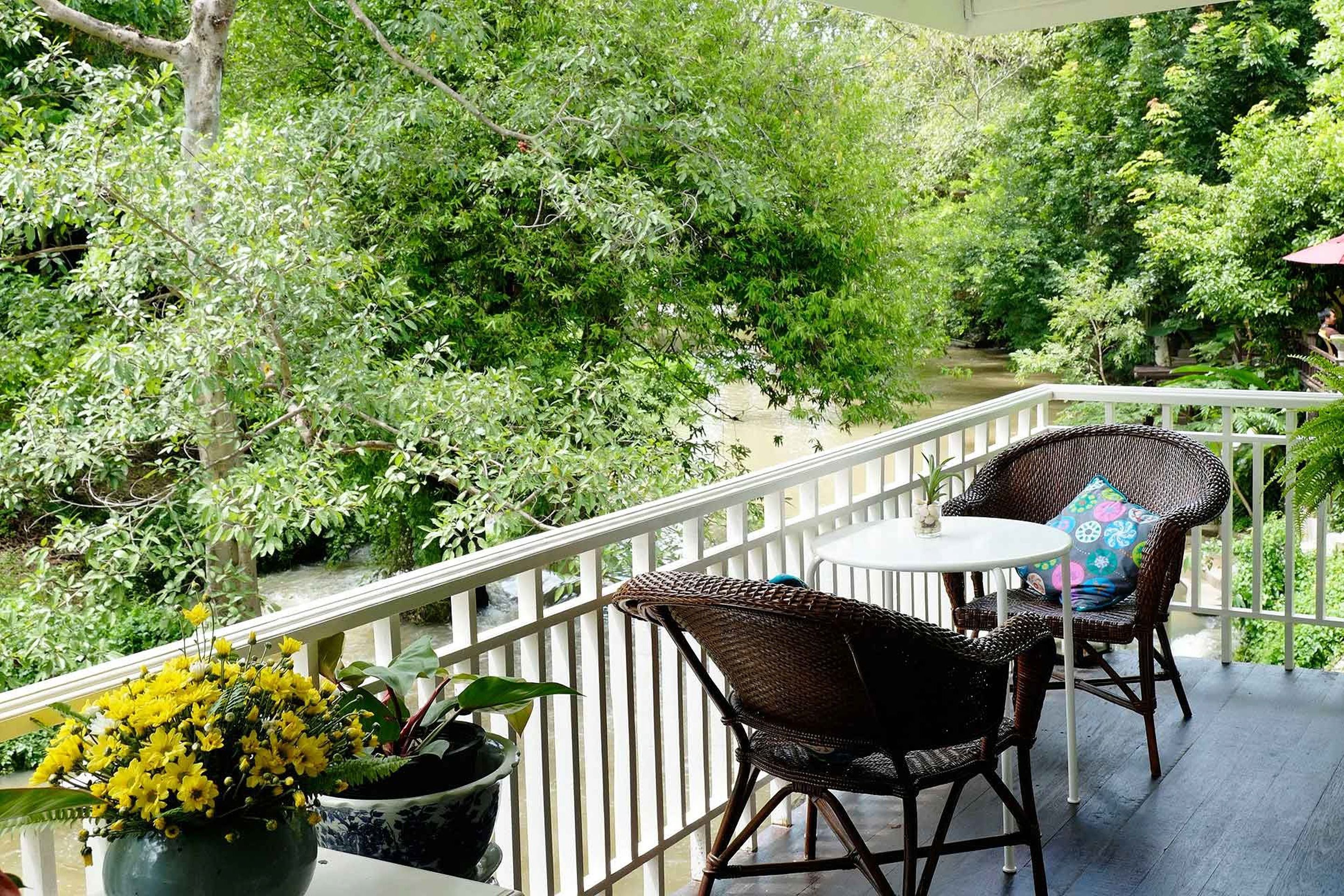 Ein Balkon mit Korbstühlen und einem kleinen Tisch, umgeben von üppiger Bepflanzung und einem Wasserspiegel.