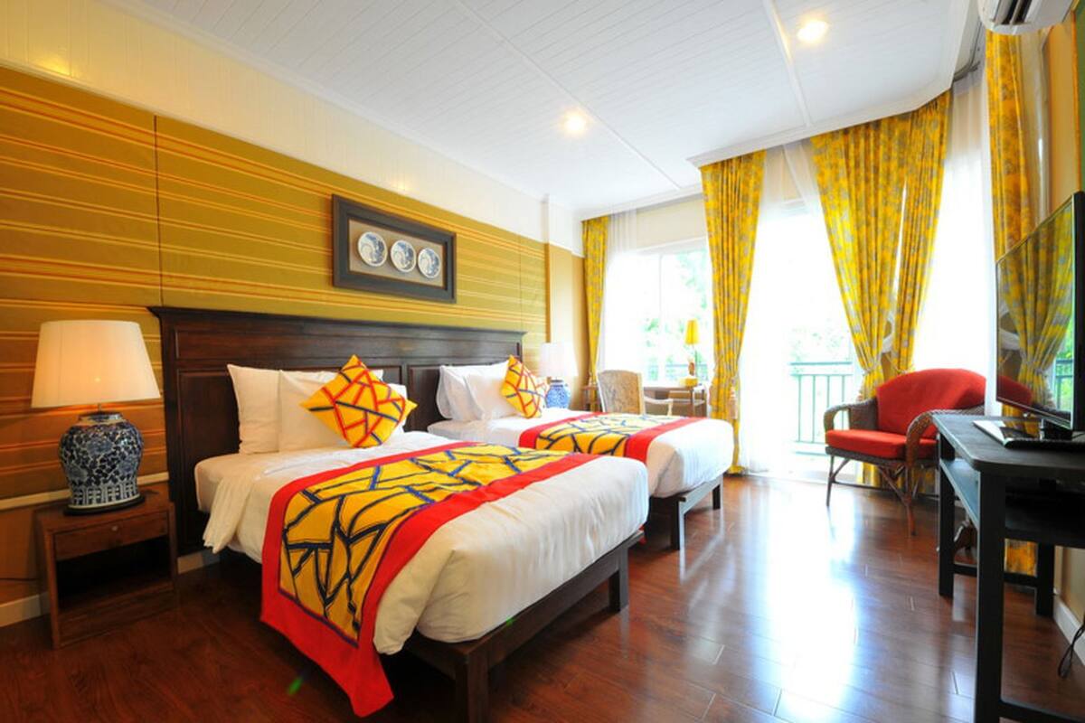 A hotel room with two beds, a desk, a chair, and a TV.
