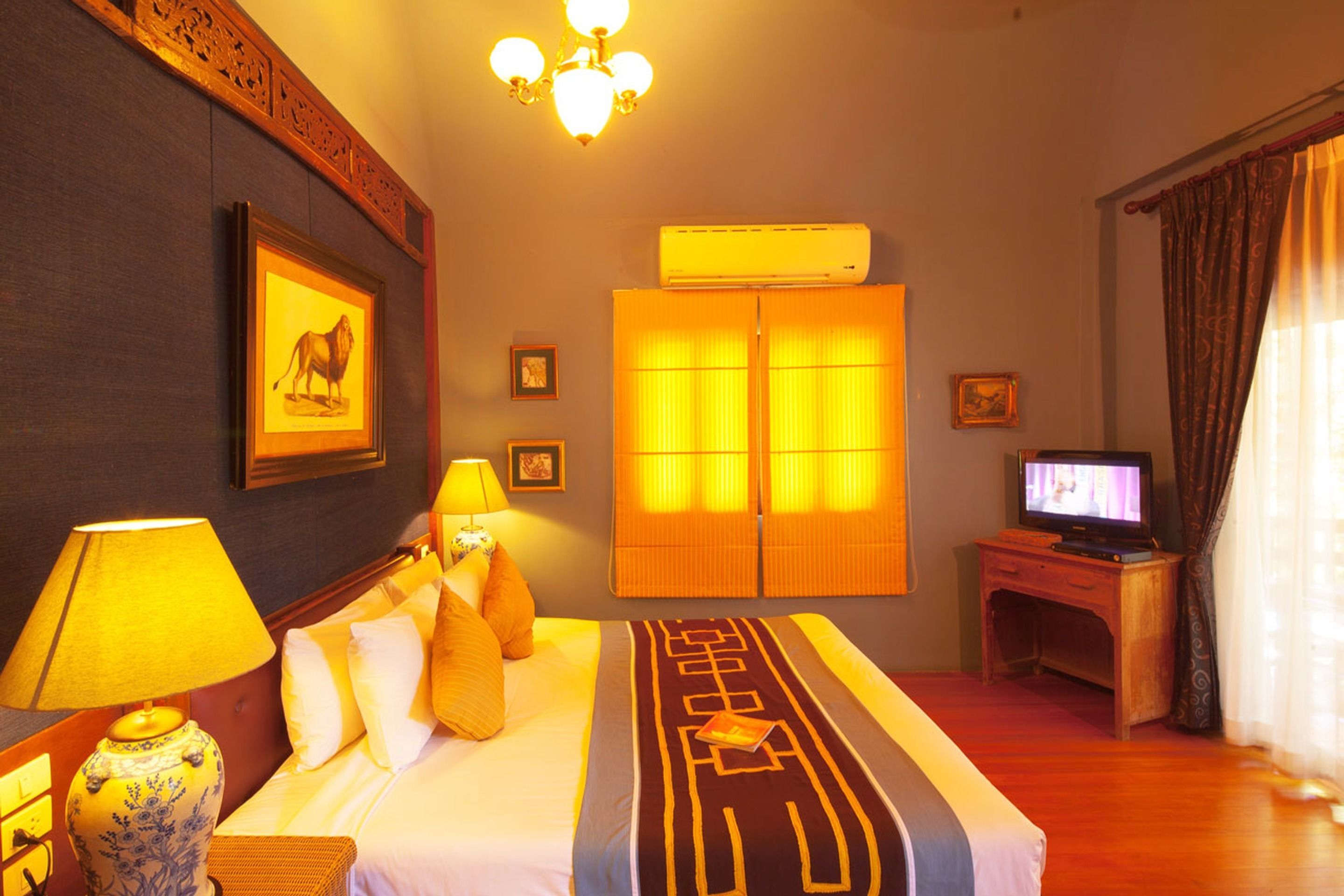 A hotel room with a bed, a television, an air conditioner, and a lamp.
