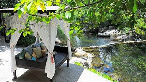 A bed with a canopy in a garden setting with a pond. - Zantiis Ndol Villas (Muak Lek)