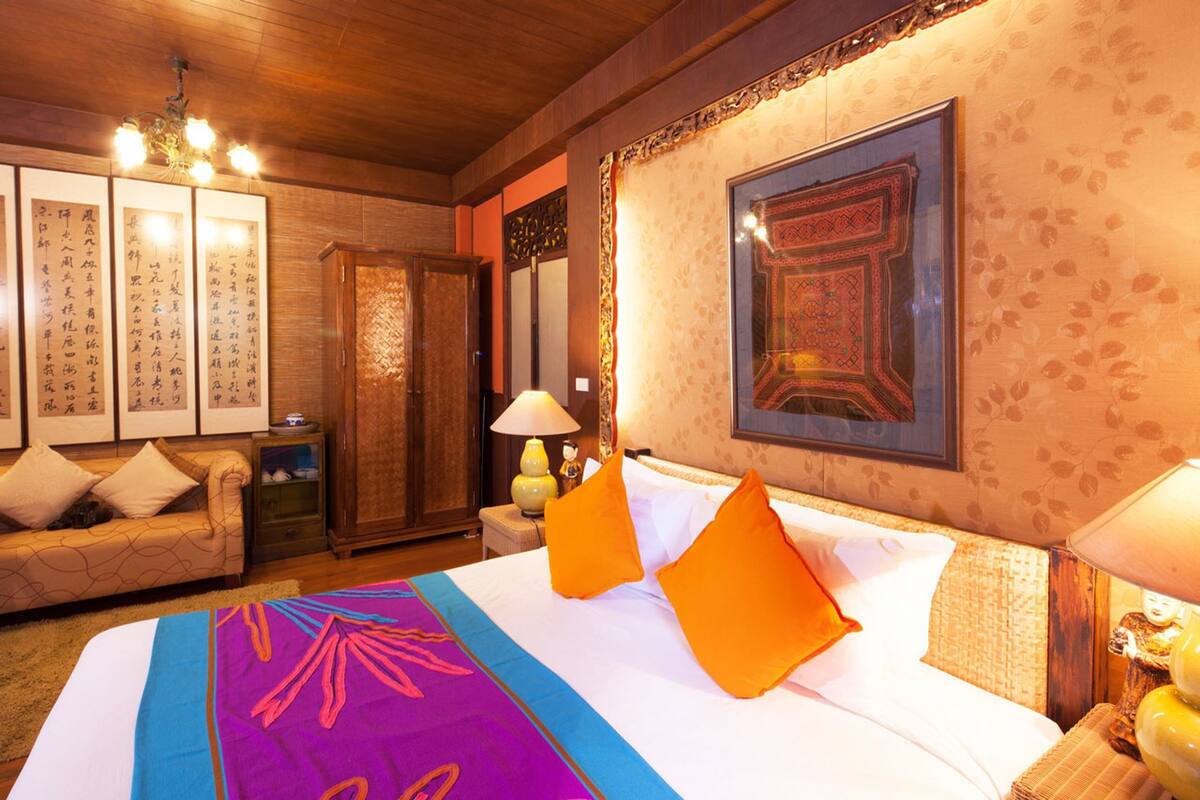 A hotel room with a large bed, a sofa, a cabinet, and framed calligraphy on the wall.
