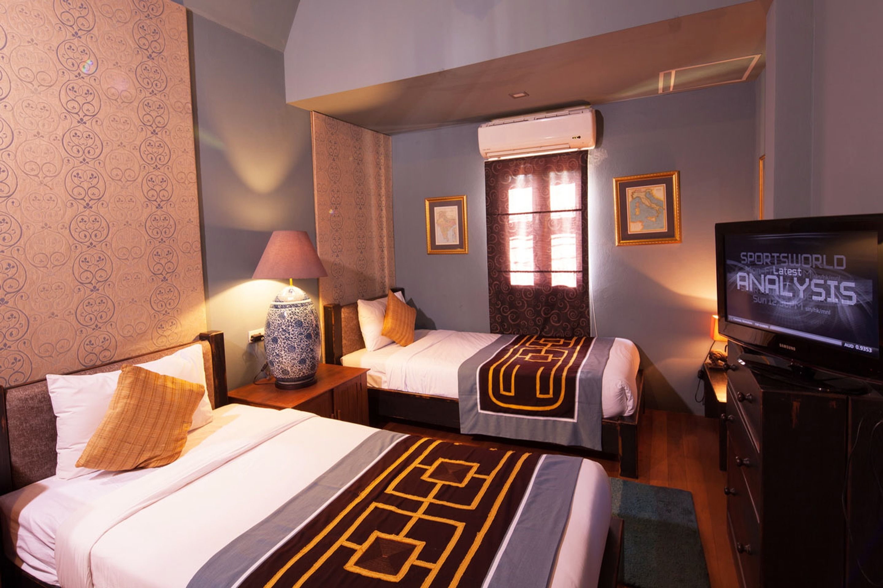 Une chambre d’hôtel avec deux lits, une télévision, une lampe et une fenêtre avec des rideaux.