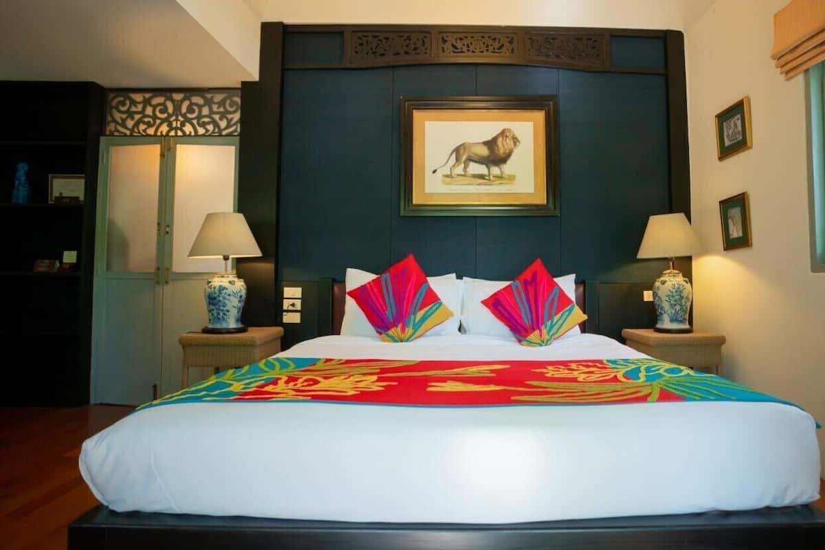 A large bed with a colorful bedspread and two decorative fans. There is a framed picture of a lion on the wall above the bed.