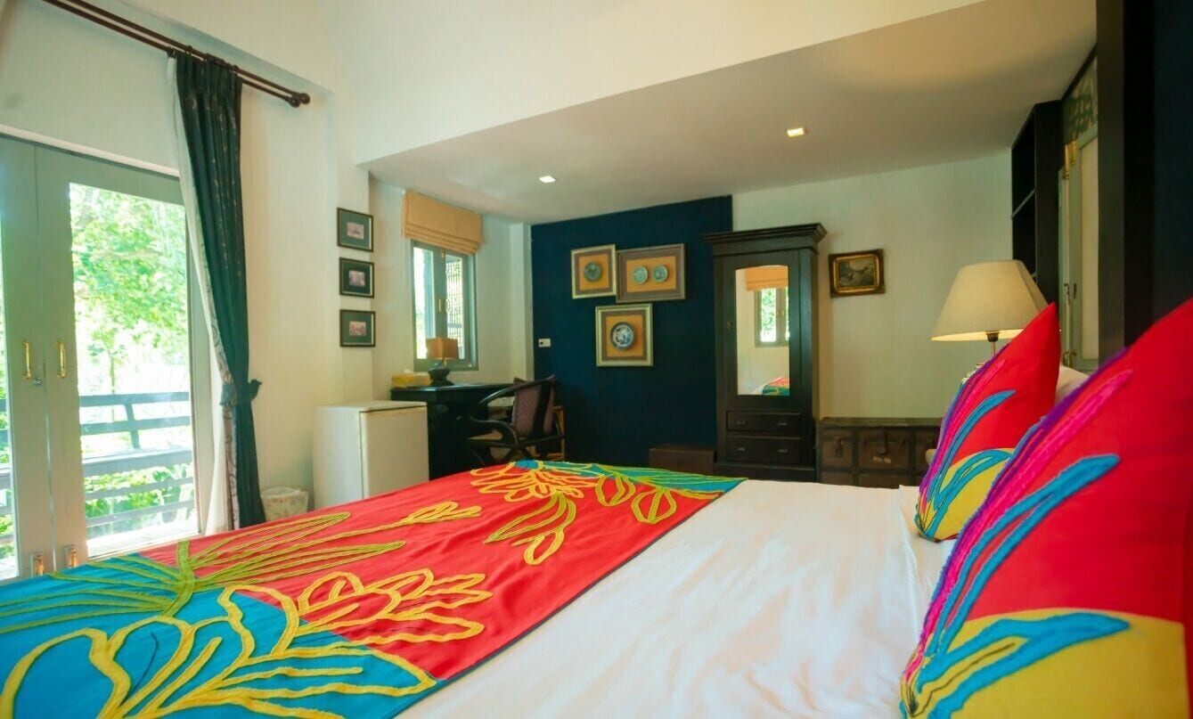 A hotel room with a bed, a desk, a chair, a lamp, and a window with curtains.