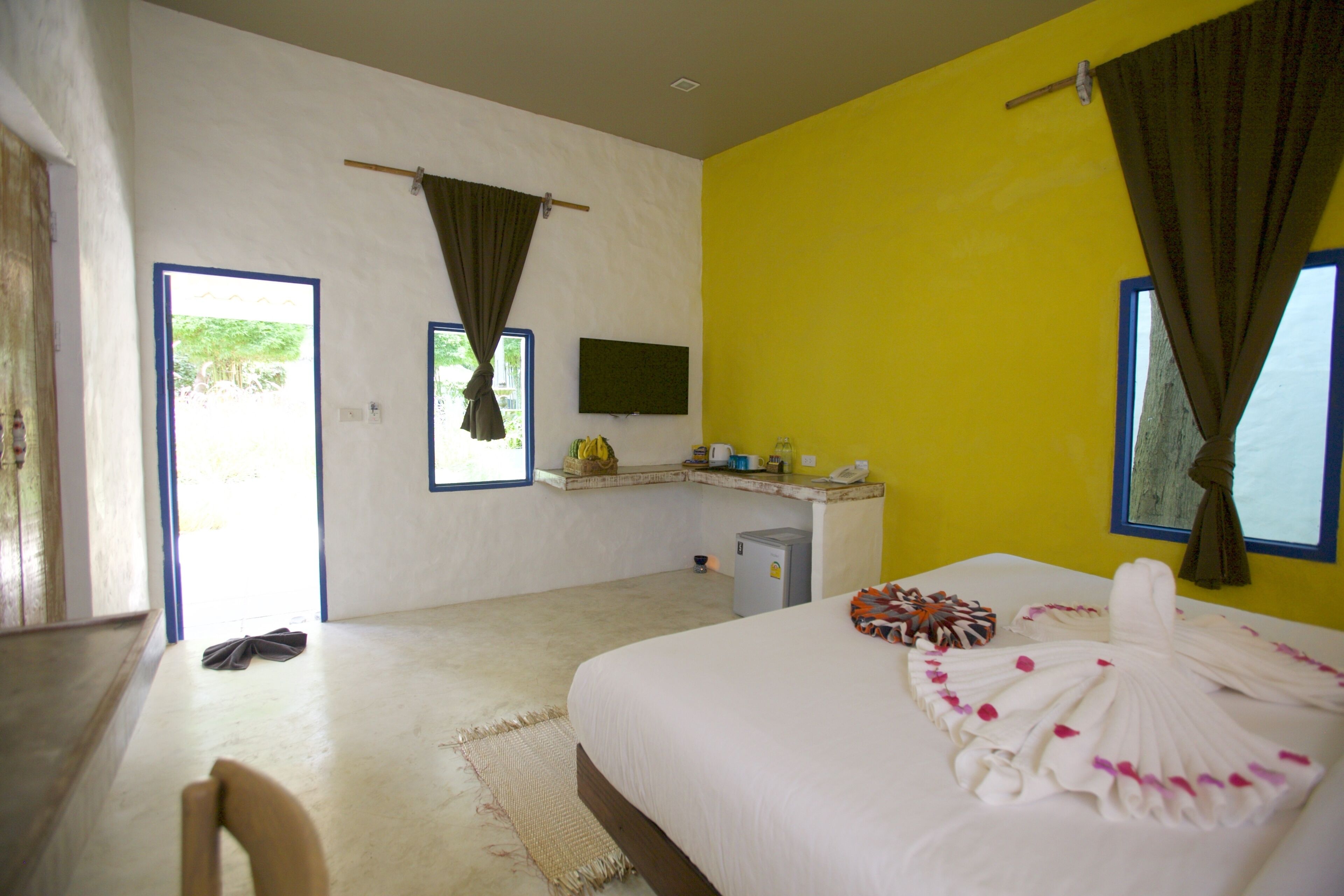 Un dormitorio con cama, escritorio, silla, un refrigerador pequeño y una ventana con cortinas.