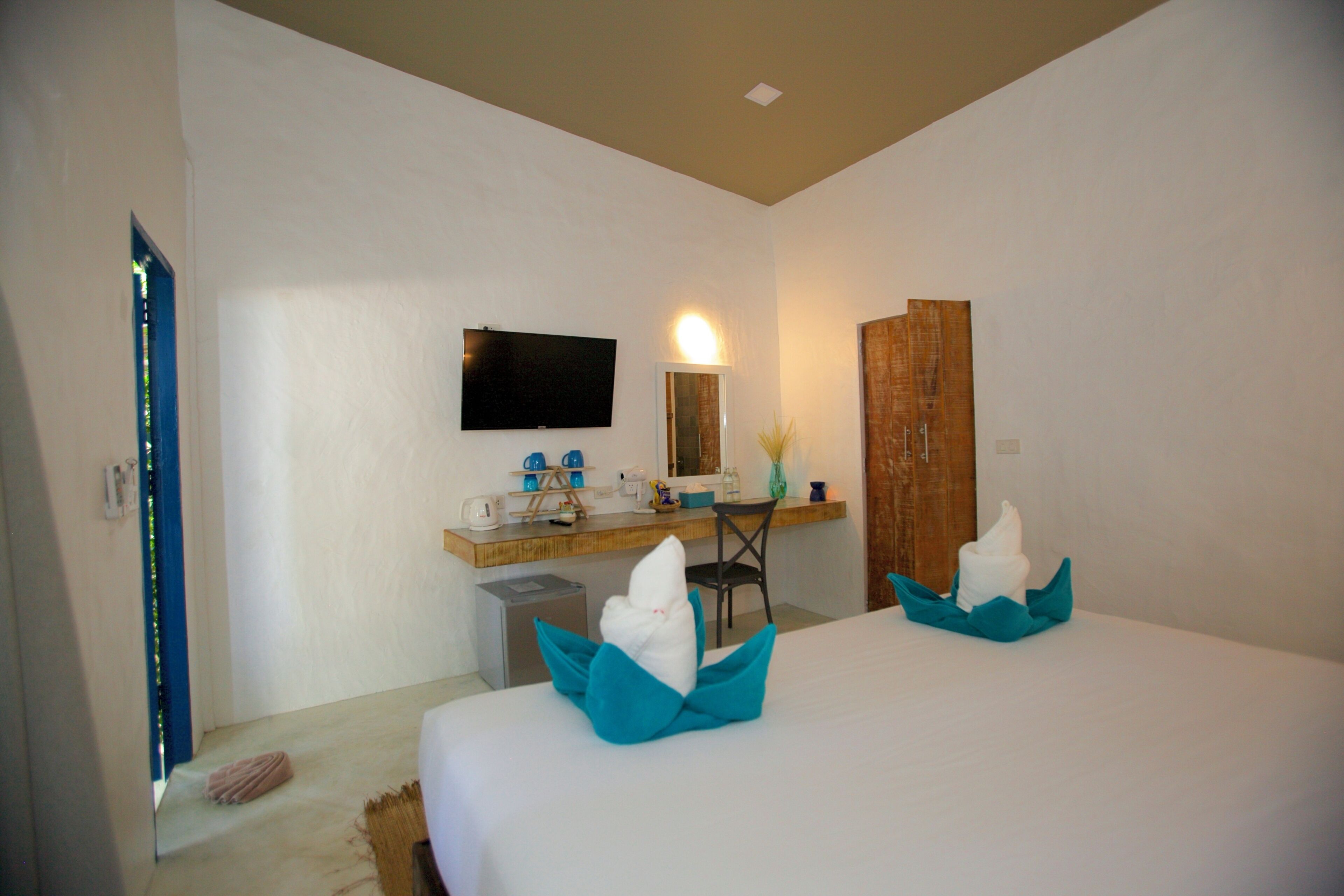 A hotel room with two beds, a desk with a flat-screen TV, a mirror, and a wooden door.
