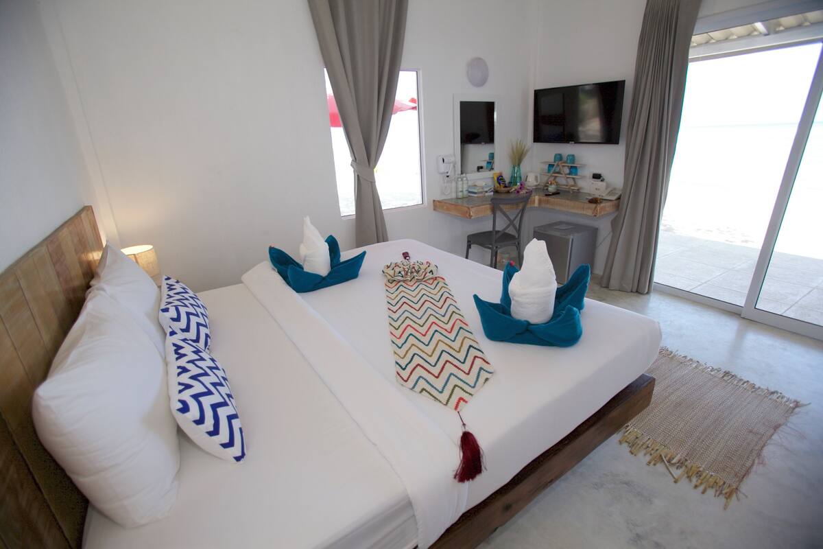 Ein Hotelzimmer mit Bett, Schreibtisch, Fernseher und Blick auf den Strand.