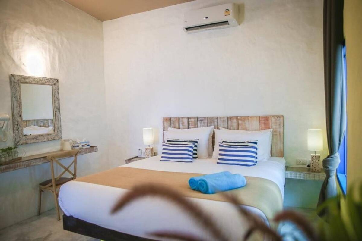 Ein Hotelzimmer mit Bett, Nachttischen, einem Spiegel, einer Klimaanlage und einem Fenster mit Vorhängen.