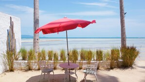 A beachside setting with a table and two chairs under a red umbrella, palm trees, and a view of the sea. - Lime & Soda Beachfront Resort (Ko Pha-ngan)