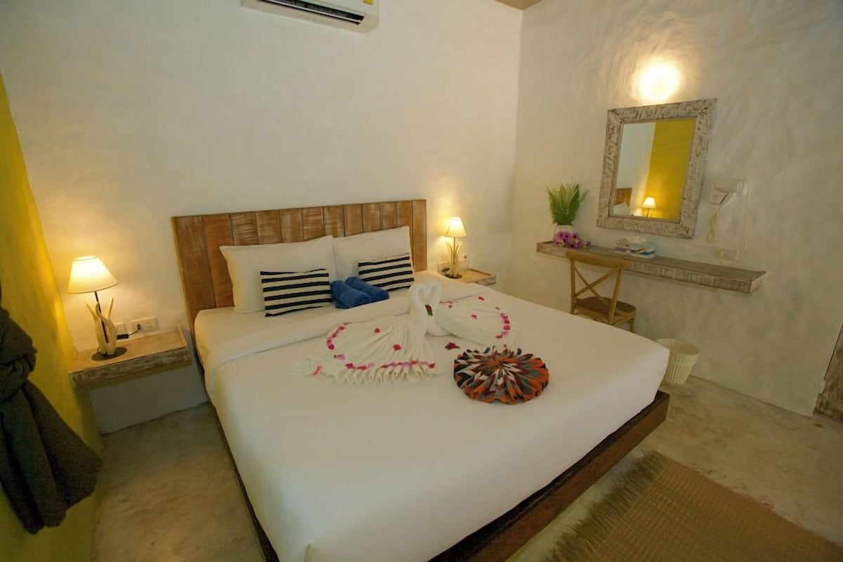 A hotel room with a bed, bedside lamps, a nightstand, a mirror, and a small table with a plant.