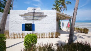 A white building with a sign reading "LIME 1" and a covered outdoor seating area with a view of the beach and ocean. - Lime & Soda Beachfront Resort (Ko Pha-ngan)