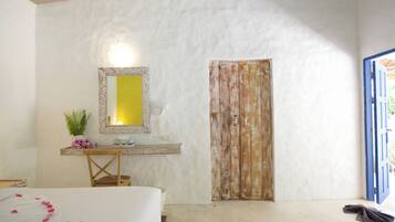 A bedroom with a bed, a desk with a mirror, a plant, and a wooden door.