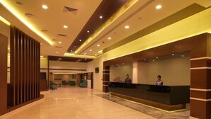 Zona de recepción de hotel con piso de mármol pulido, mostrador de recepción y área de descanso con sillas.