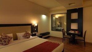 Una habitación de hotel con una cama grande, mesitas de noche, un escritorio con una silla, un espejo y una pequeña mesa con frutas.