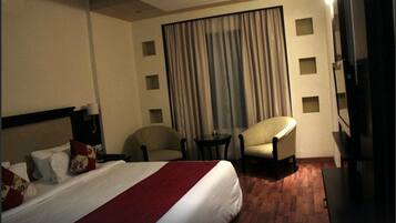 Une chambre d’hôtel avec un grand lit, deux fauteuils, une petite table et un téléviseur.