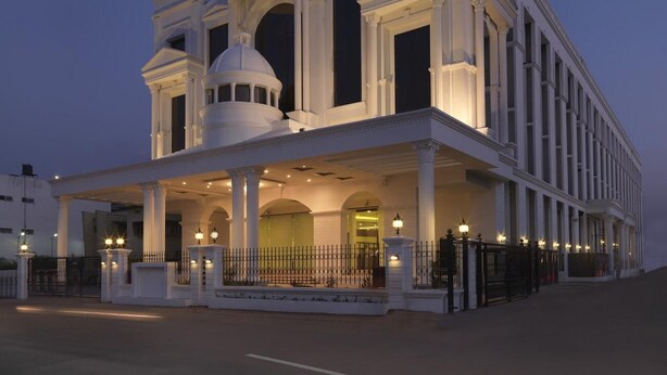 Un edificio imponente con una cúpula central y múltiples columnas, que presenta una entrada cubierta y un camino de acceso con portones.