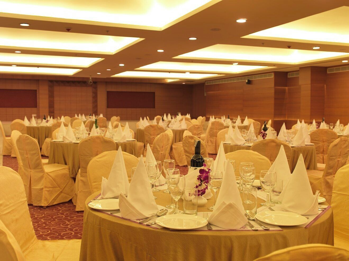 Une salle de banquet avec des tables rondes dressées pour le repas, recouvertes de nappes blanches et entourées de chaises dorées.