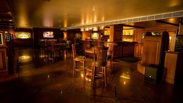 Zona de bar con poca luz, muebles de madera y una pantalla de televisión.
