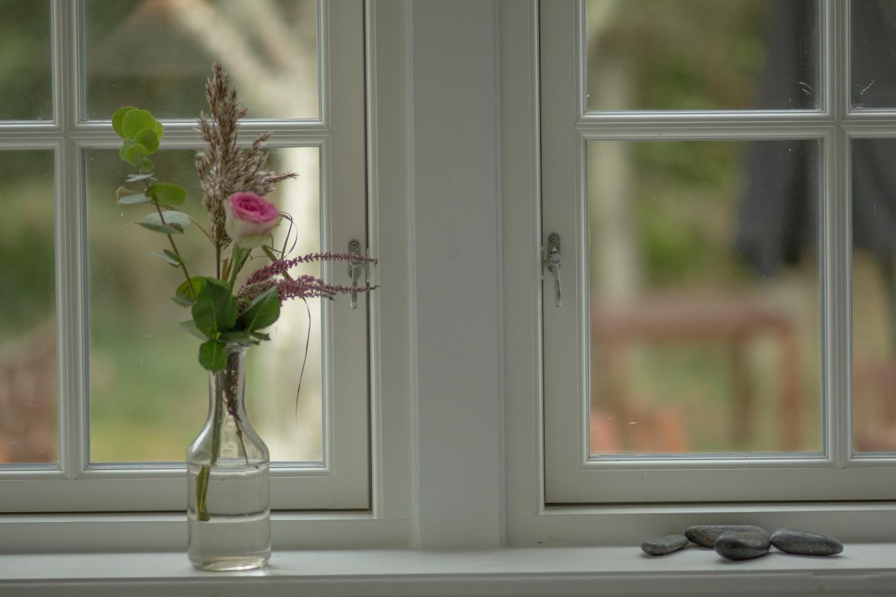 A clear view of a window with a vase containing a pink rose and other flowers on a windowsill.