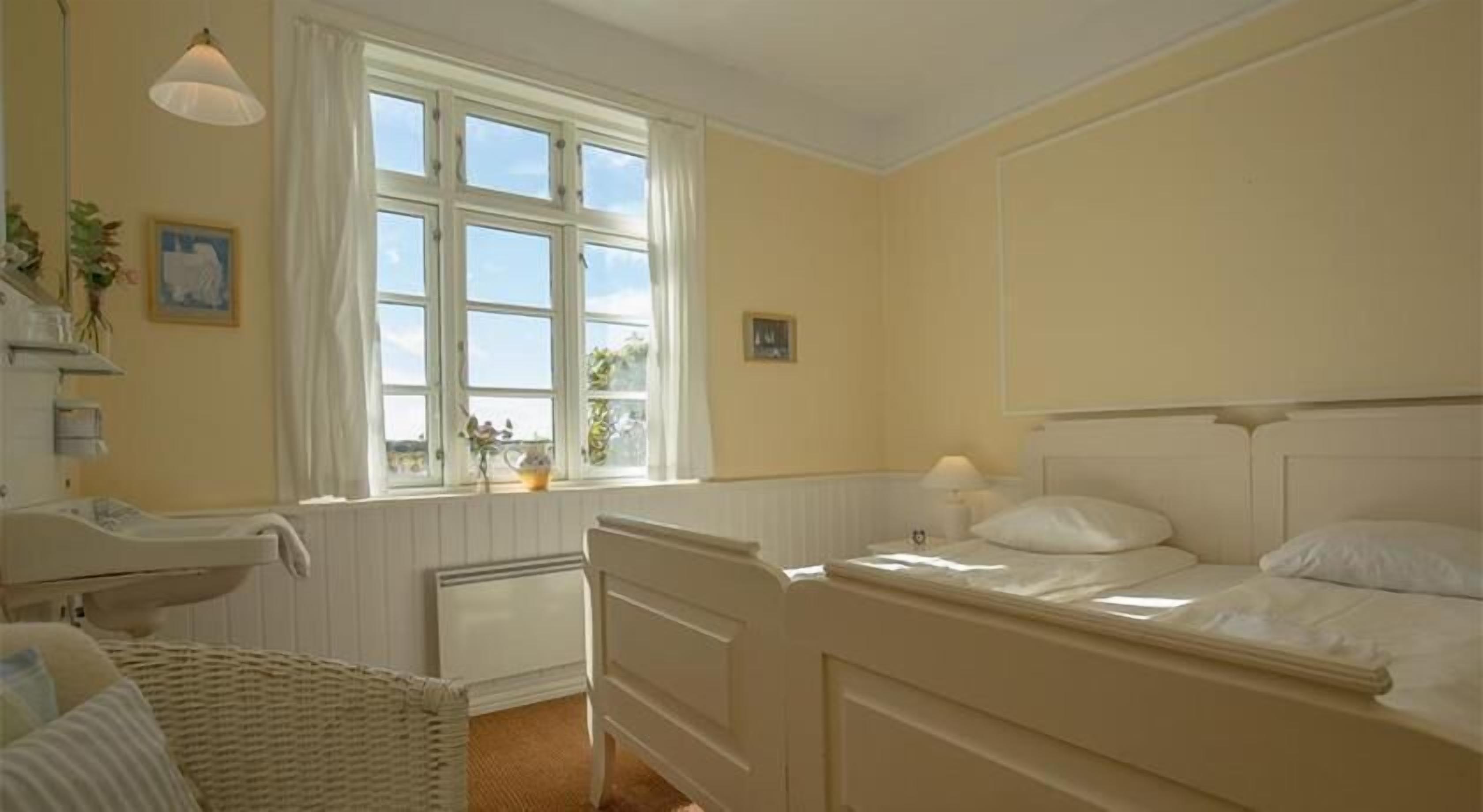 A room with a bed, a bedside table, a chair, a window, and a radiator.