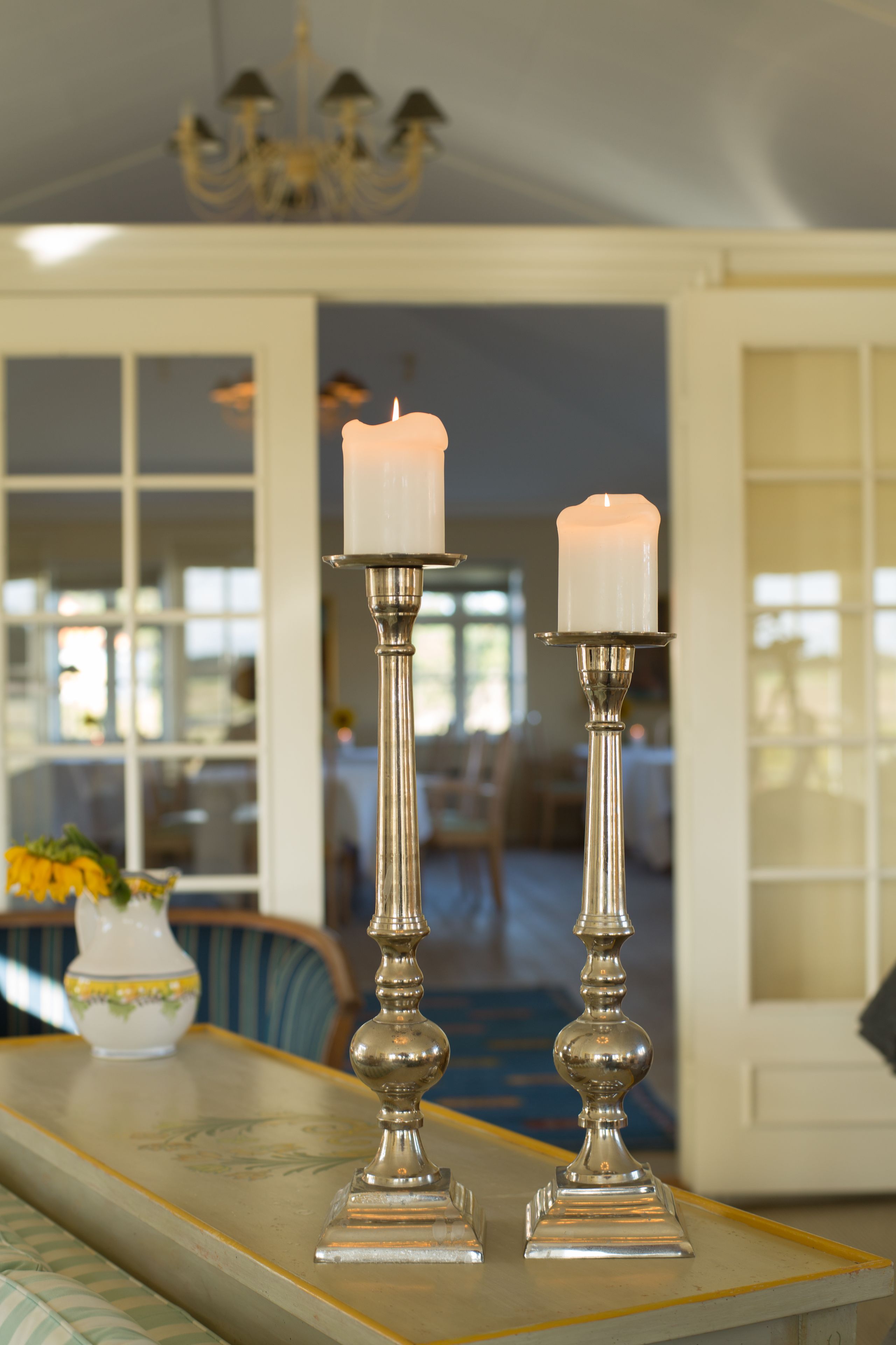 Two candle holders with candles on a table in a room with a chandelier.