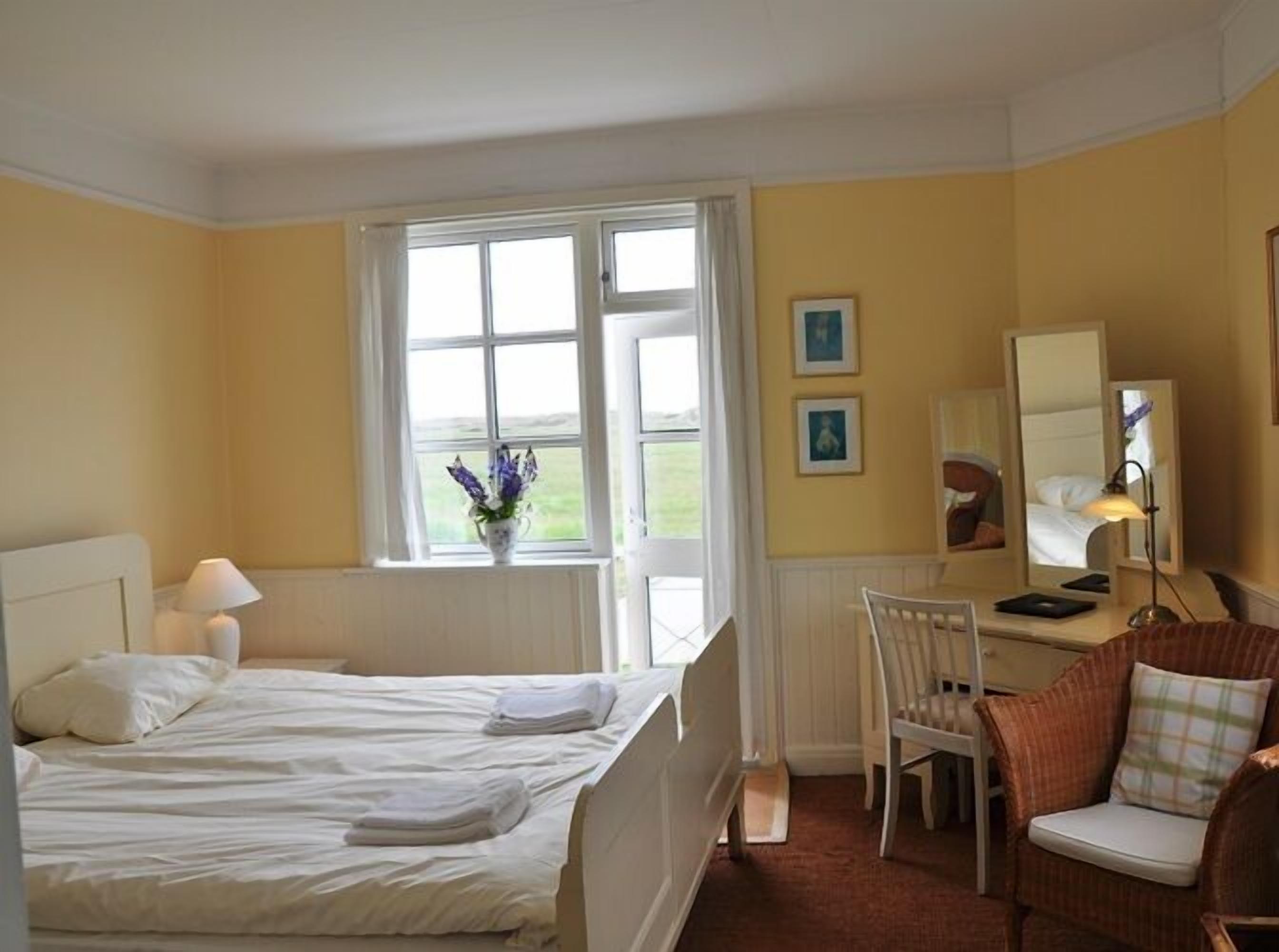 A hotel room with a bed, a chair, a desk, a lamp, and a window with a view.