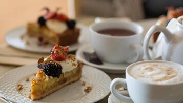 Un plato de postre con una porción de tarta cubierta de bayas y crema batida, una taza de café y una tetera sobre una mesa.