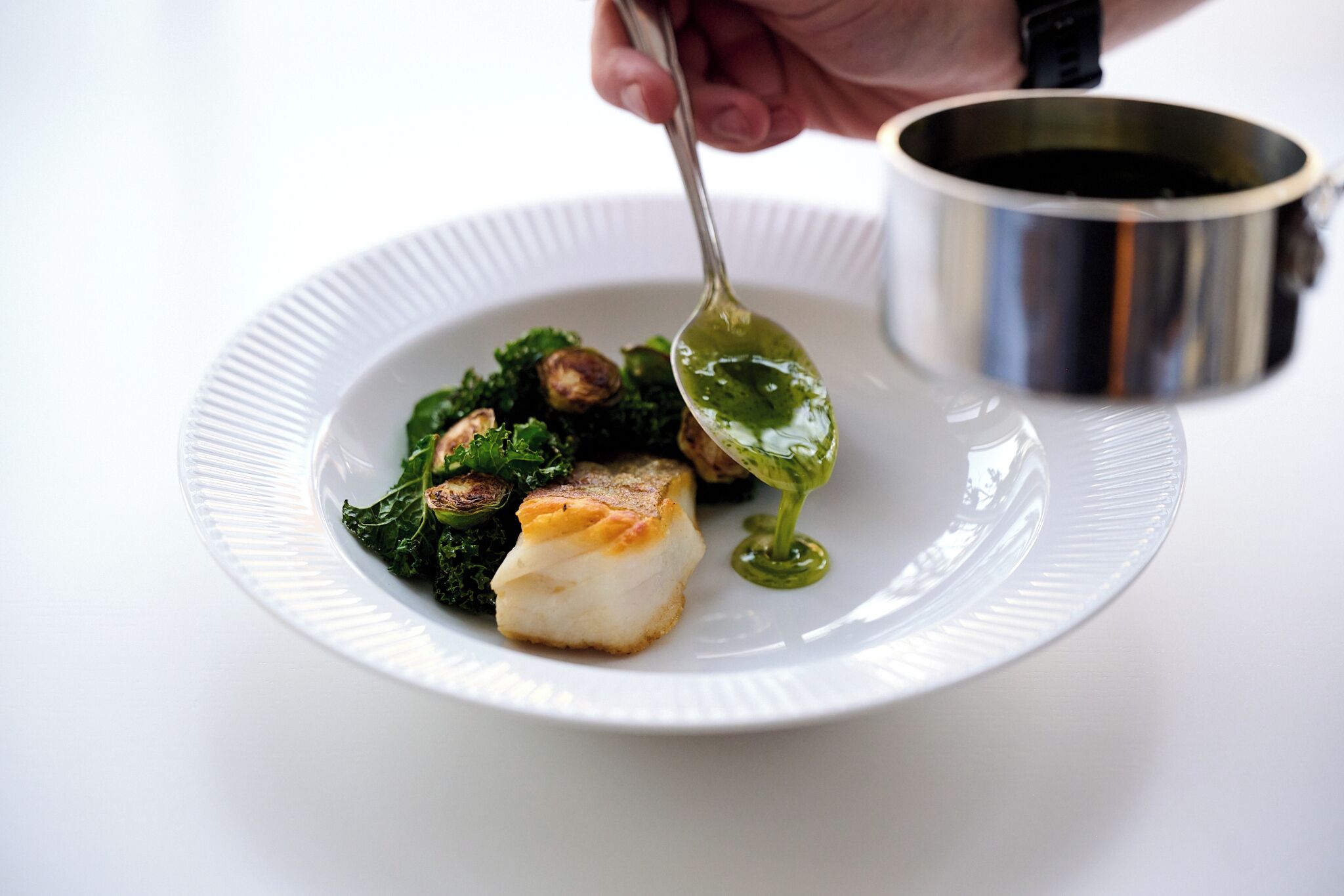 Ein Teller mit Fisch, Gemüse und Pilzen, sowie ein Löffel mit Soße.
