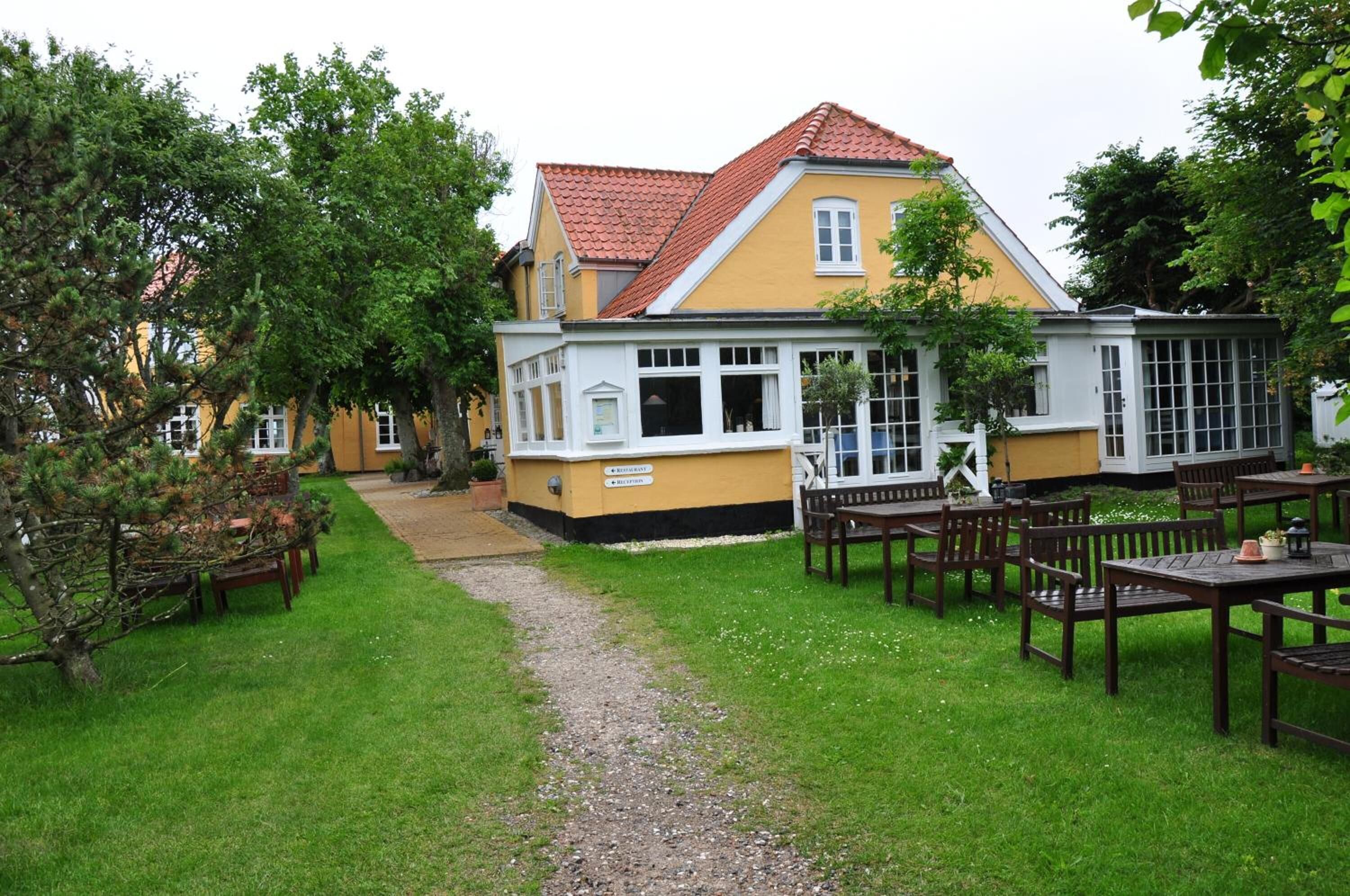 A yellow building with a red roof, surrounded by a grassy area with wooden tables and chairs.